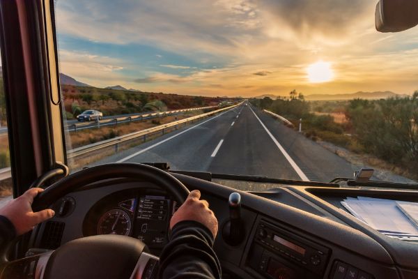 View from the driver's seat of a truck of the highway and a landscape of fields at dawn.