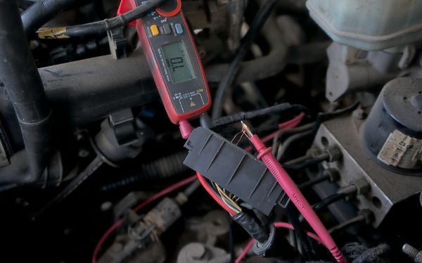 An auto electrician using diagnostic tools to test voltage levels in a car's electrical system