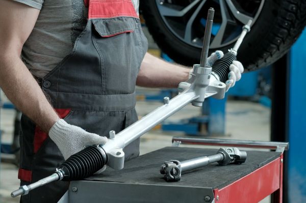 An auto mechanic holds a new steering rack to fix a vehicle's steering system