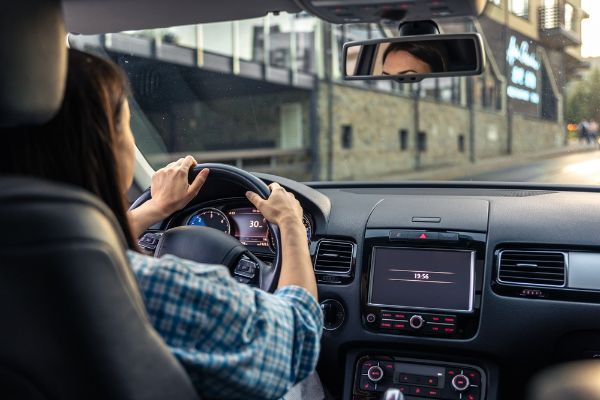 Woman driving a car, hands on the wheel close-up, view from the back to the road.