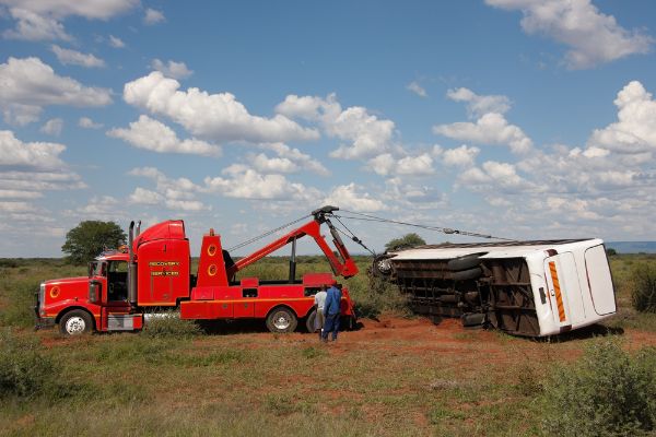 tow truck lifting an overturned bus on the roadside in the bush