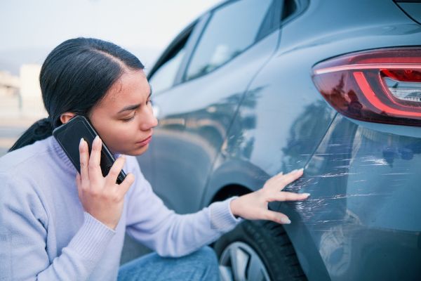 Woman calling auto repair shop examining car damage
