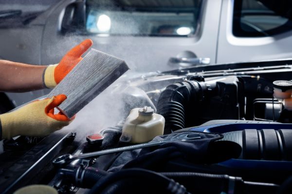 A mechanic holds a dusty car air filter to check for air filter replacement