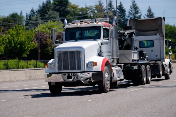 big rig semi truck tractor tows a broken semi truck on a highway