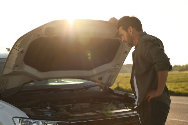 Upset man looking under hood of broken car outdoor