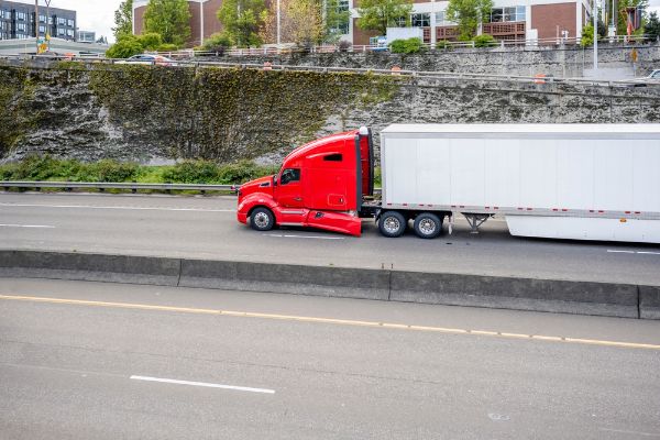 Loaded classic big rig industrial red semi truck tractor with broken fender transporting commercial