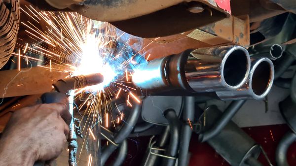 Mechanic is fixing a vehicles muffler system by welding the exhaust pipe