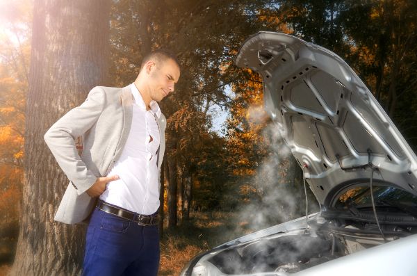 Car breakdown. Man standing on the road by the broken car in the middle of nowhere. Hood opened,