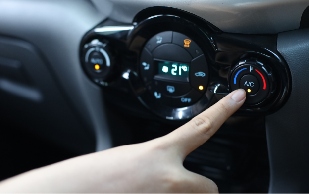 A hand presses the air conditioning button on the console of a car.