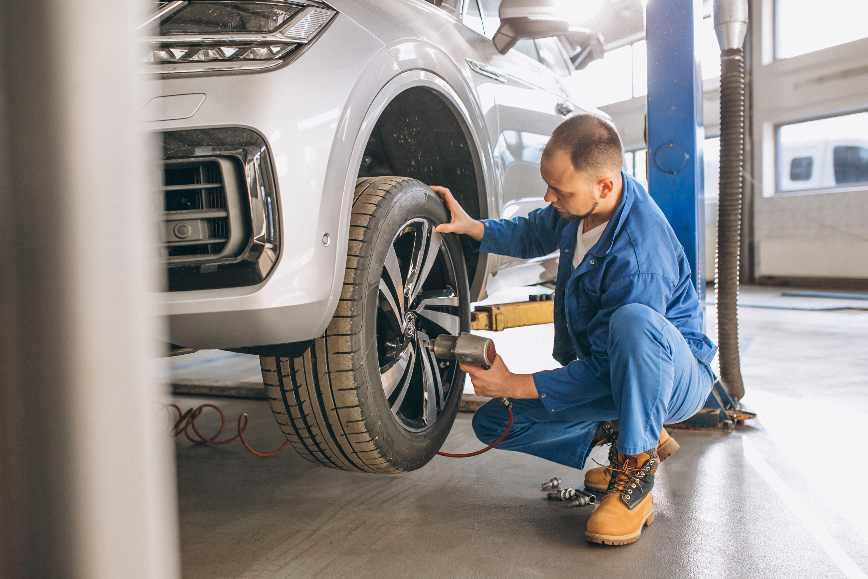 Man using a tool to assess a lifted vehicle's suspension system around the tire.