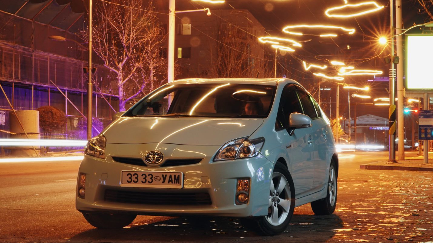 A modern Toyota Prius under neon lights in a city.