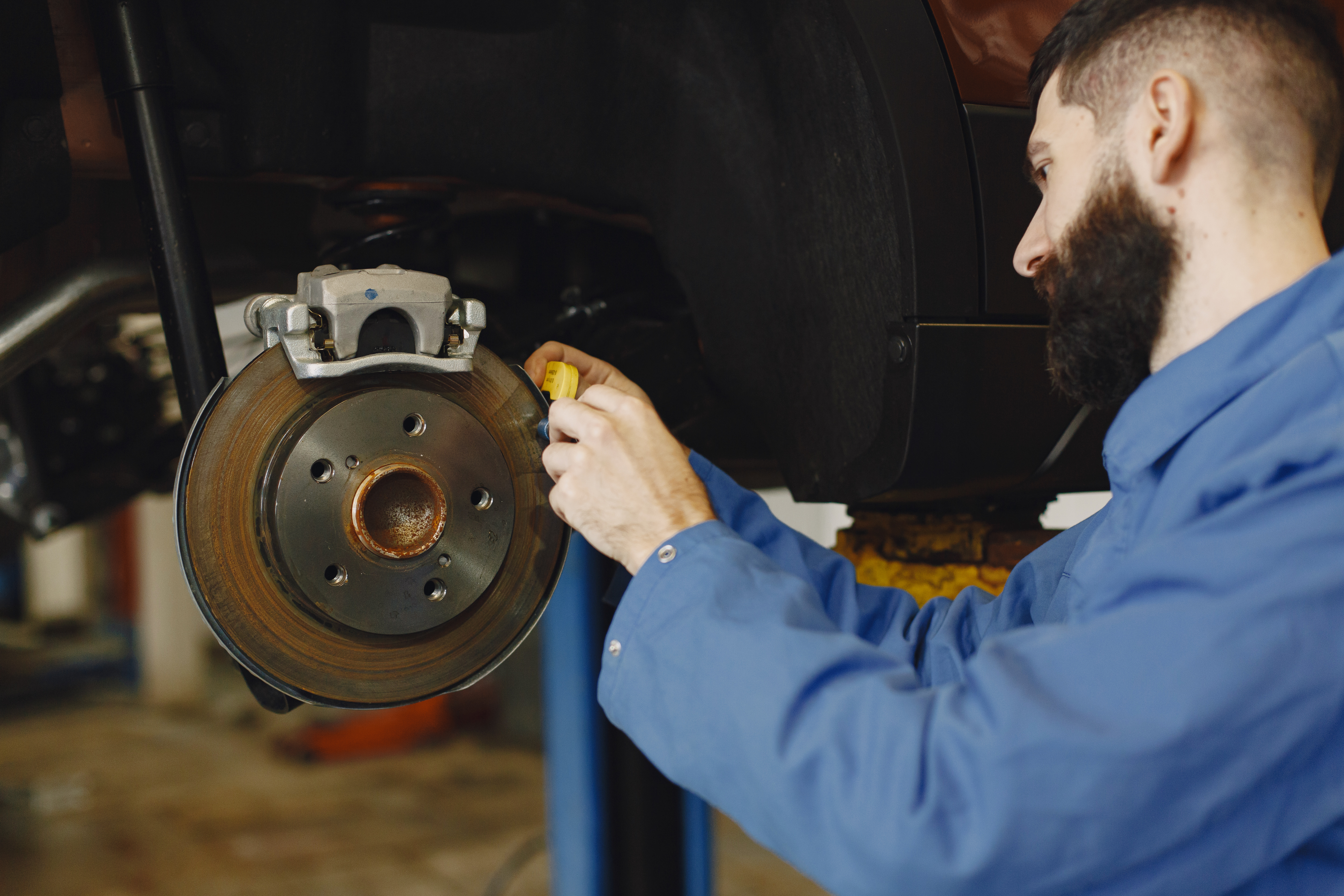 Close-up of a mechanic in blue work clothes using a tool on a wheel.