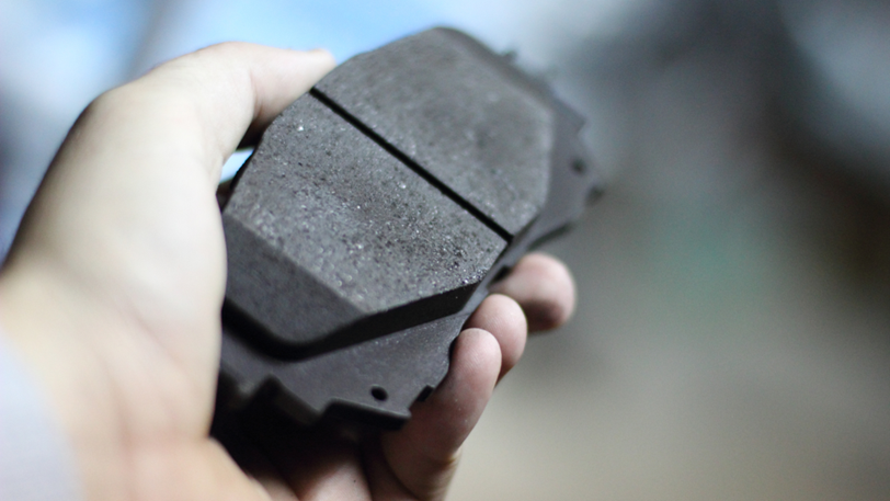 A person holds a new brake pad in his hand, ready to install.